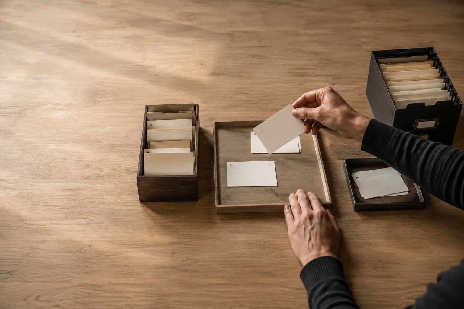 Une personne examine des fiches sur une table d'atelier, entre une boîte d'arrivée, un plateau de sélection et une boîte d'archives